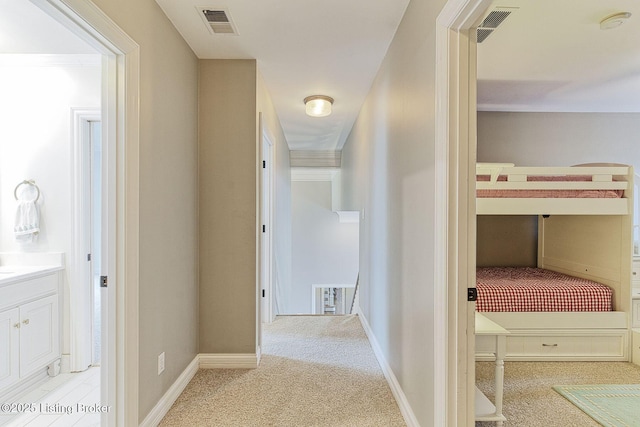 hallway with visible vents, light colored carpet, and baseboards