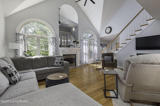 living area with wood finished floors, stairway, ceiling fan, a tile fireplace, and high vaulted ceiling