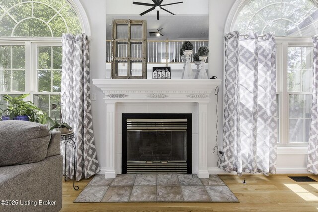living area with wood finished floors, ceiling fan, a fireplace, baseboards, and visible vents