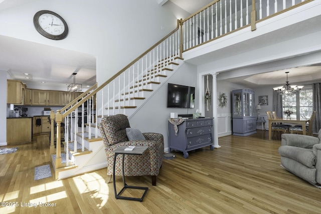 living area featuring a chandelier, light wood-type flooring, a towering ceiling, and stairway