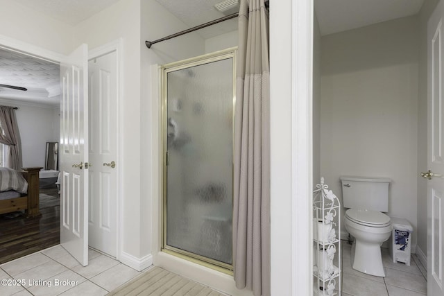 bathroom with a shower stall, tile patterned flooring, baseboards, and toilet