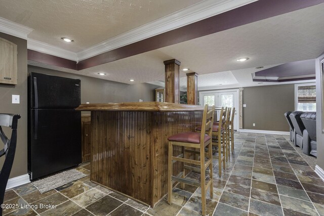 kitchen with crown molding, a textured ceiling, stone tile flooring, baseboards, and freestanding refrigerator