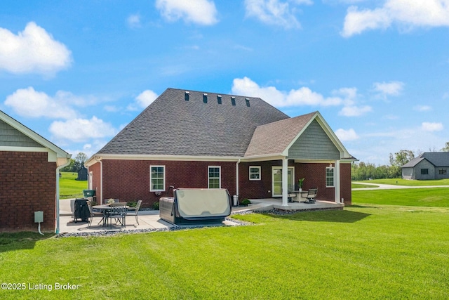 rear view of property with brick siding, a yard, a patio, and a shingled roof