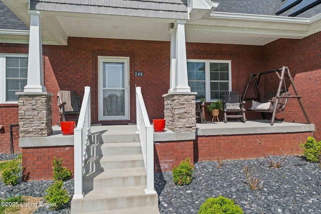 view of exterior entry with brick siding and a porch