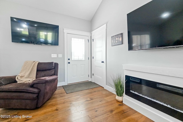 foyer entrance featuring vaulted ceiling, hardwood / wood-style floors, a glass covered fireplace, and baseboards