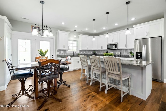 kitchen with white cabinets, stainless steel appliances, visible vents, a kitchen island, and decorative backsplash