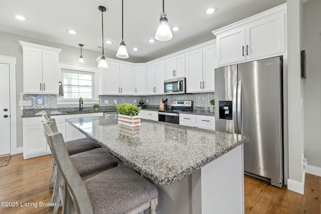 kitchen with white cabinets, stainless steel appliances, a sink, decorative backsplash, and wood finished floors