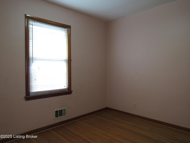 empty room featuring visible vents, dark wood finished floors, and baseboards