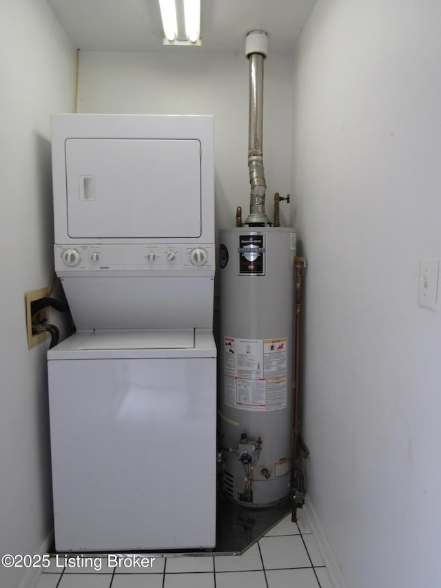 clothes washing area featuring water heater, stacked washer / drying machine, laundry area, light tile patterned floors, and baseboards