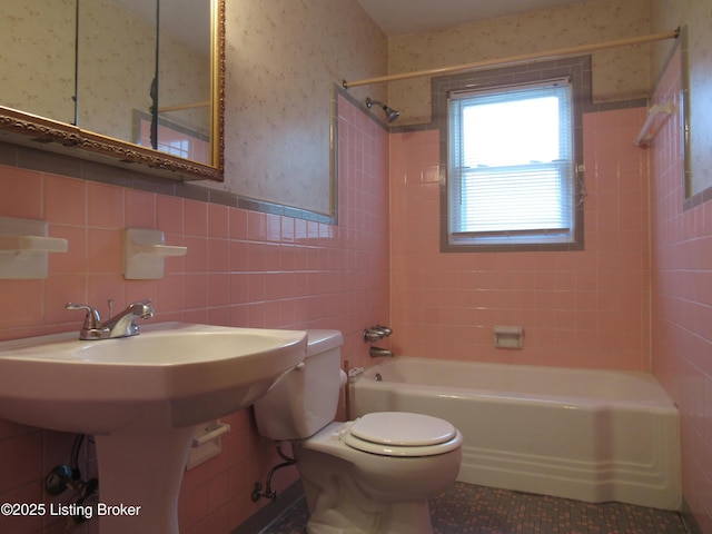 bathroom featuring a wainscoted wall, tub / shower combination, toilet, tile walls, and tile patterned floors