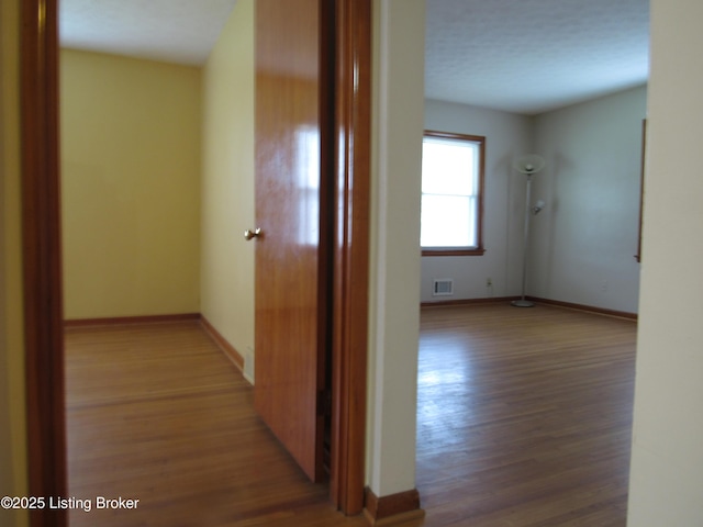 hallway with visible vents, wood finished floors, and baseboards