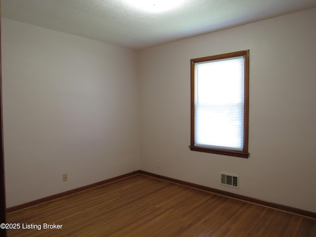 empty room with baseboards, visible vents, and wood finished floors