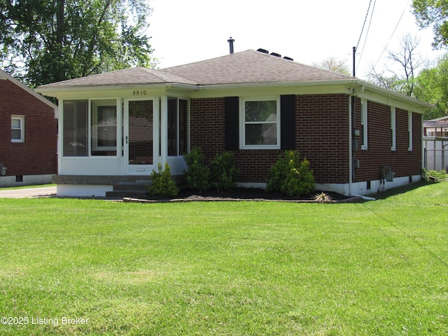 single story home with a front yard, a shingled roof, brick siding, and a sunroom