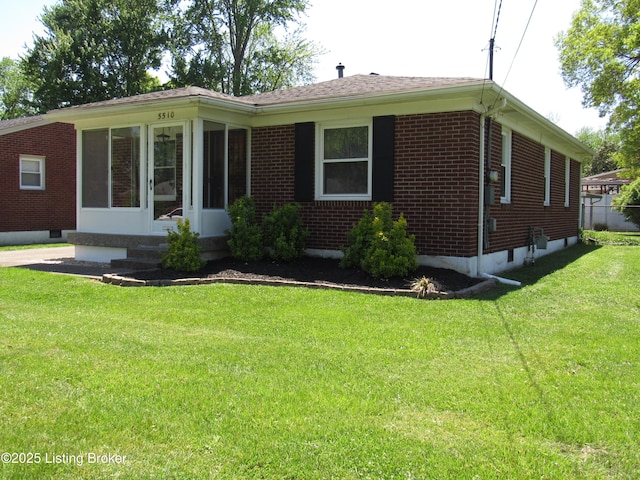 view of front of house featuring brick siding, a front yard, and a sunroom