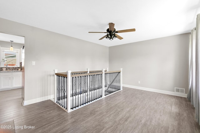 spare room with wood finished floors, visible vents, a ceiling fan, and baseboards