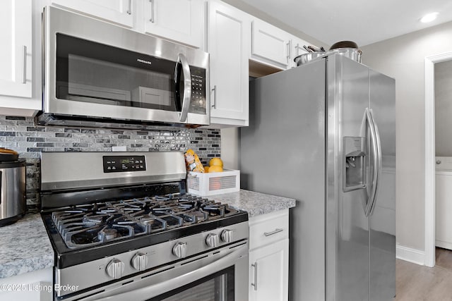 kitchen with stainless steel appliances, backsplash, light stone countertops, light wood-style flooring, and white cabinetry