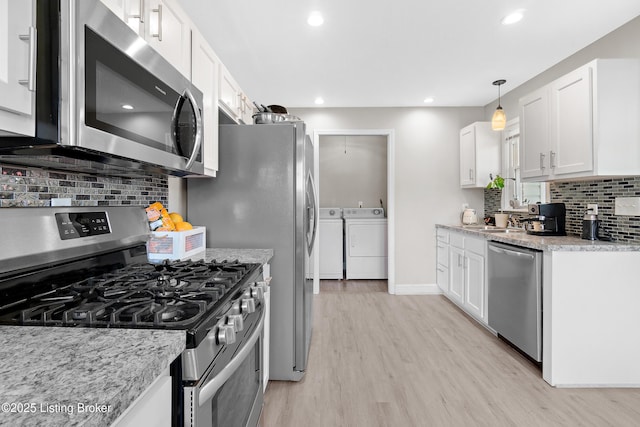 kitchen featuring light wood-style flooring, washing machine and dryer, white cabinetry, decorative backsplash, and appliances with stainless steel finishes