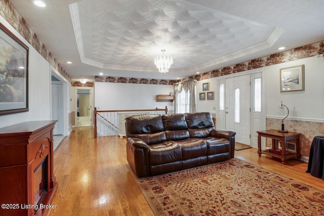 living area featuring light wood finished floors, an inviting chandelier, recessed lighting, crown molding, and a raised ceiling