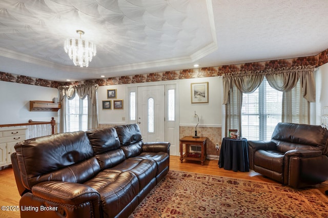 living room with a wainscoted wall, a chandelier, wood finished floors, ornamental molding, and a raised ceiling