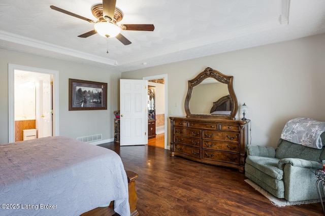 bedroom featuring a tray ceiling, visible vents, a ceiling fan, wood finished floors, and ensuite bath