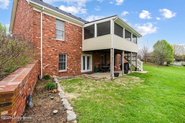 rear view of property featuring brick siding, a sunroom, a yard, and a patio