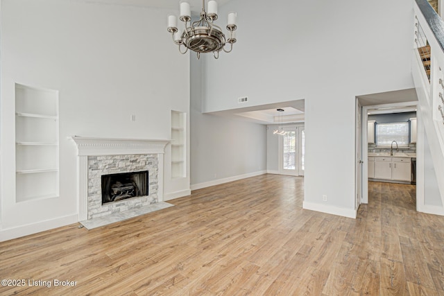 9003 Holly Village Ct, Lyndon, KY 40242 - unfurnished living room featuring light wood-type flooring, a towering ceiling, an inviting chandelier, built in shelves, and a stone fireplace