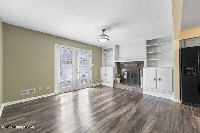 unfurnished living room with dark wood finished floors, a fireplace, baseboards, visible vents, and french doors