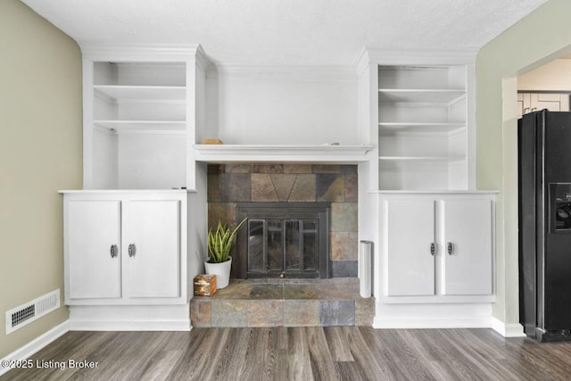 unfurnished living room featuring wood finished floors, visible vents, a tiled fireplace, and baseboards