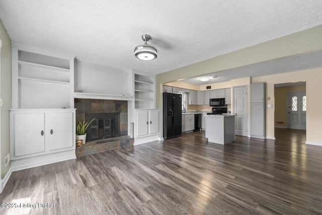 unfurnished living room featuring a stone fireplace, dark wood-style flooring, a textured ceiling, and baseboards