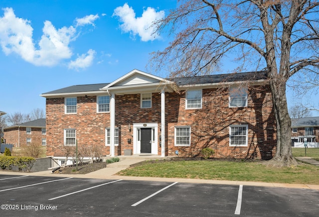 multi unit property with brick siding, a front lawn, and uncovered parking