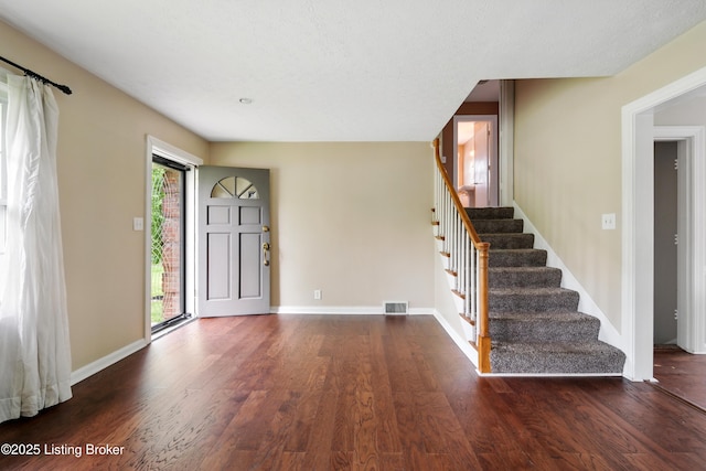 entryway with dark wood finished floors, visible vents, stairs, and baseboards