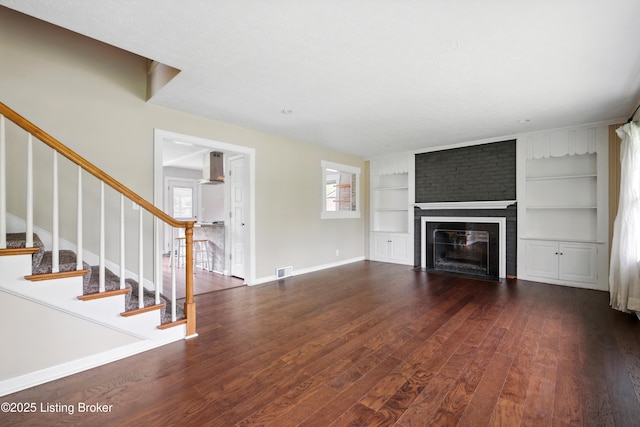 unfurnished living room featuring wood finished floors, stairs, built in features, a brick fireplace, and visible vents