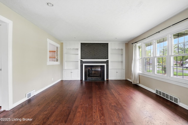 unfurnished living room with a brick fireplace, visible vents, dark wood finished floors, and baseboards