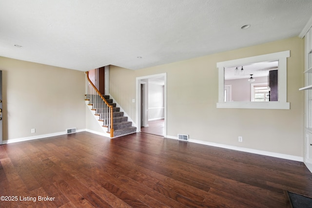 unfurnished living room featuring baseboards, visible vents, wood finished floors, and stairs