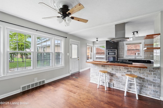 kitchen featuring island exhaust hood, visible vents, wood finished floors, and baseboards