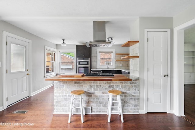 kitchen with dark wood-style floors, stainless steel double oven, island exhaust hood, a breakfast bar area, and backsplash
