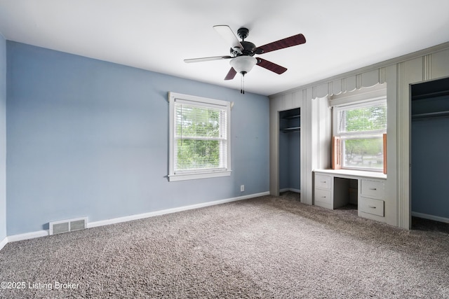 unfurnished bedroom featuring carpet, visible vents, two closets, and multiple windows