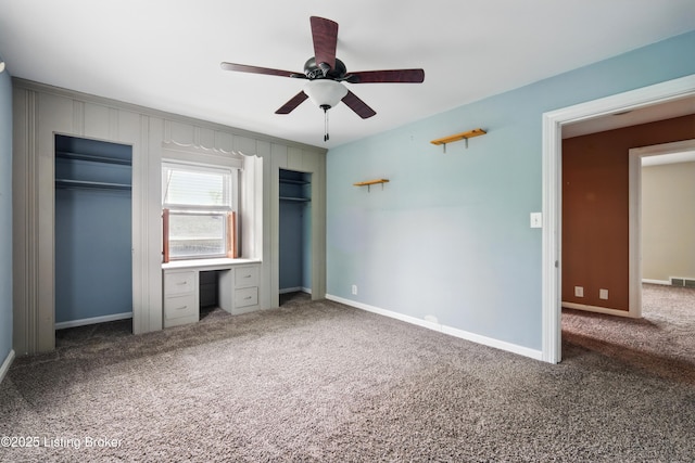 unfurnished bedroom with two closets, carpet, built in study area, visible vents, and a ceiling fan