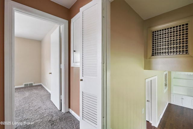 hall with dark colored carpet, visible vents, and baseboards