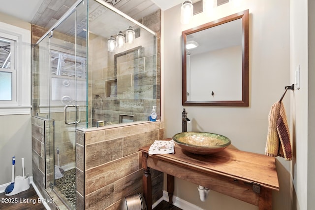 bathroom with baseboards, a stall shower, wood finished floors, and a sink