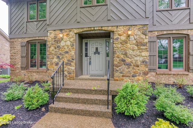 view of exterior entry with central AC, brick siding, and stone siding