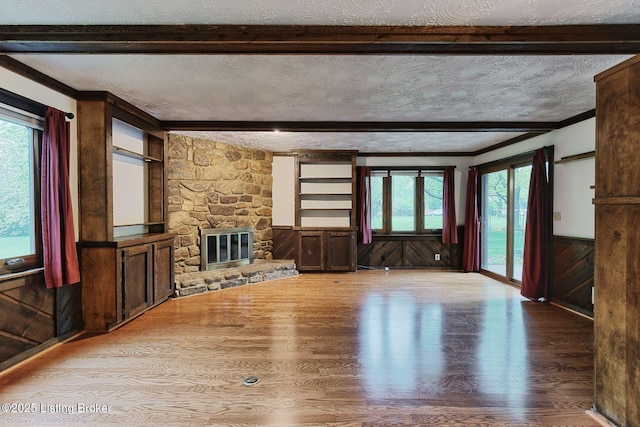 unfurnished living room featuring beam ceiling, a fireplace, a wainscoted wall, a textured ceiling, and wood finished floors