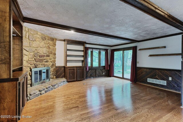 unfurnished living room featuring a fireplace, visible vents, a textured ceiling, wainscoting, and wood finished floors