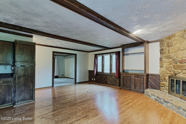 unfurnished living room featuring beam ceiling, a textured ceiling, wood finished floors, and a fireplace