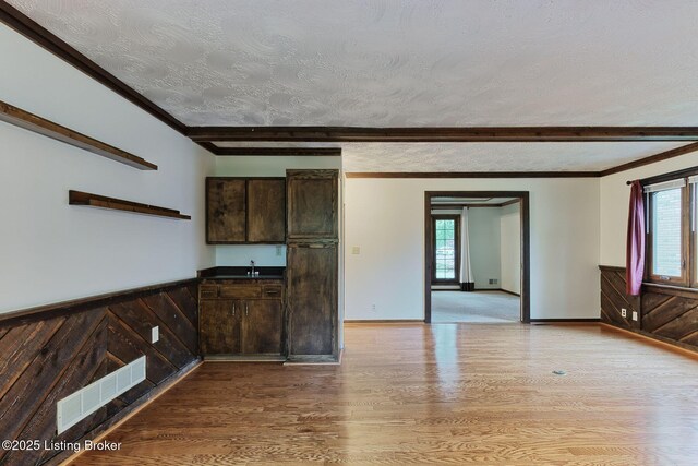 unfurnished room with a sink, beamed ceiling, visible vents, and wood finished floors