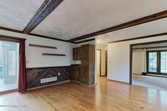 unfurnished living room with beam ceiling, a textured ceiling, visible vents, and light wood-style flooring