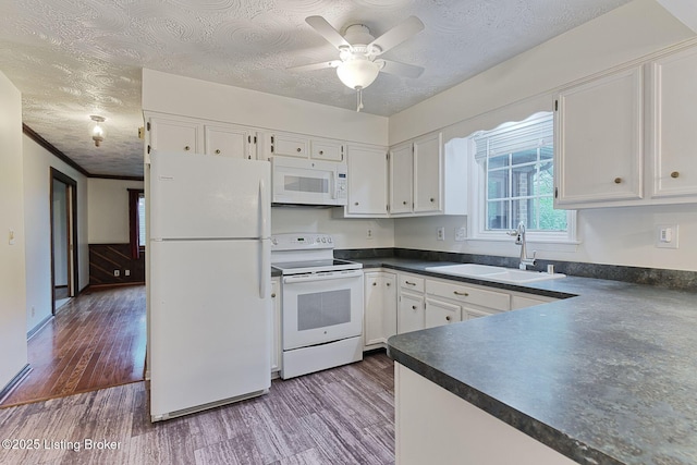 kitchen with dark countertops, white appliances, white cabinets, and a sink