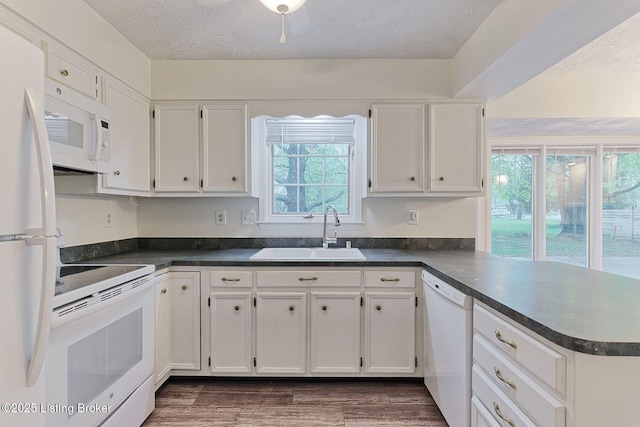kitchen featuring dark countertops, a sink, and white appliances