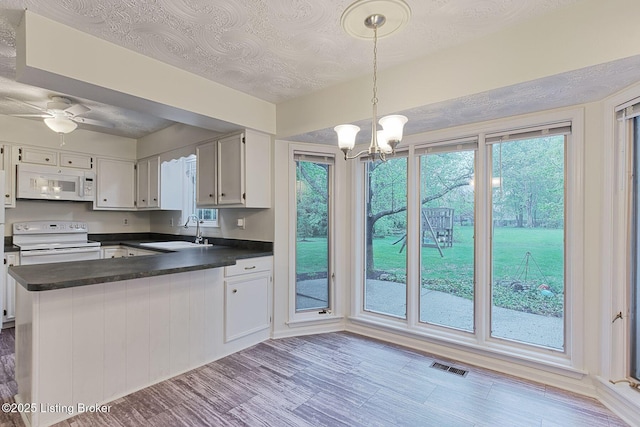 kitchen with a sink, dark countertops, visible vents, white appliances, and a peninsula