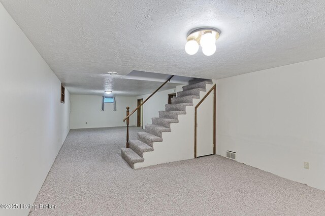 below grade area featuring a textured ceiling, visible vents, stairs, and carpet floors